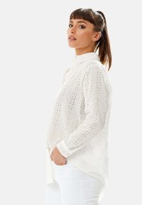 White blouse featuring a collared neckline, eyelet pattern, and long sleeves. The fabric is lightweight with a slightly loose fit.
