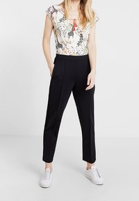 Vit blommig blus med korta ärmar, svarta skräddarsydda byxor och vita sneakers. Har en fyrkantig halsringning och röda detaljer.