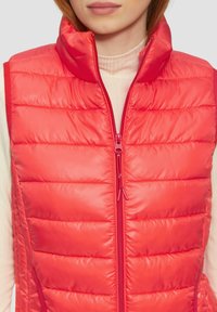Rode puffervest met een hoge kraag en een rits aan de voorkant. Bevat gequiltte secties en een gladde, glanzende textuur. Ideaal voor het laagjesprincipe.