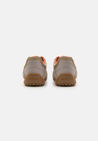 Grå og beige sneakers med oransje detaljer, med et mesh-overdel og gummisåle, som viser en teksturert finish og merkevarelogo.