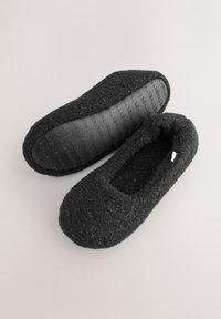 Pantofole in feltro nero con parte superiore testurizzata e suola in gomma nera liscia con il nome del marchio impresso. Design piatto e arrotondato.