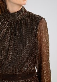 Abito lungo a maniche lunghe in bronzo plissettato con colletto alto e vita sottile, caratterizzato da una finitura metallica testurizzata e maniche trasparenti.