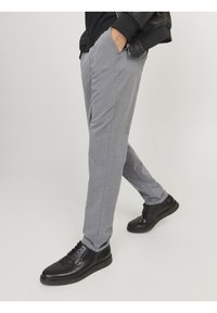 Pantalons gris ajustés avec une texture lisse, des poches avant et une coupe slim. Portés avec des chaussures à lacets noires.