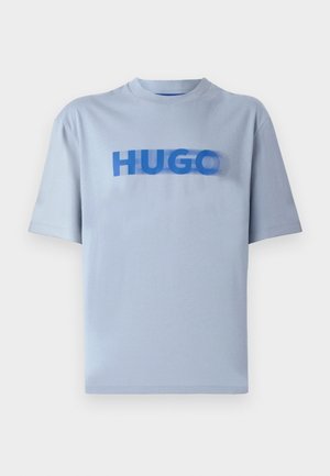 Svetlo modra majica s kratkimi rokavi iz bombaža, ki na sredini prikazuje drzen moder grafični napis "HUGO" v gladkem, rahlo zamehnjenem dizajnu.