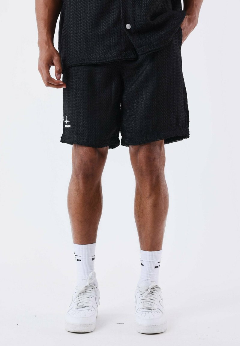 Zwarte textuur shorts met een elastische taille, een franjeszoom en witte logodetail, gecombineerd met witte sneakers en sokken.