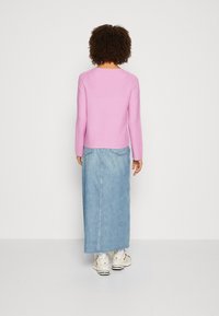 Haut à manches longues rose associé à une jupe maxi en denim bleu. La tenue présente un design simple avec des lignes épurées et une silhouette ajustée.