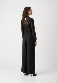 Svart blonde bodysuit med gjennomsiktige lange ermer og nøkkelhullbak, kombinert med høyt liv svarte vidde bukser og stiletto hæler.