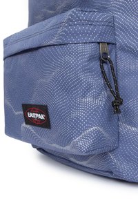 Zaino blu testurizzato con motivo a onde, dotato di tasca anteriore con zip e accenti neri, incluso un'etichetta del marchio visibile.