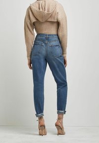 Jeans de mezclilla azul de tiro alto con un ajuste relajado, que cuentan con dos bolsillos traseros y puños desgastados, combinados con un suéter cropped beige de canalé.