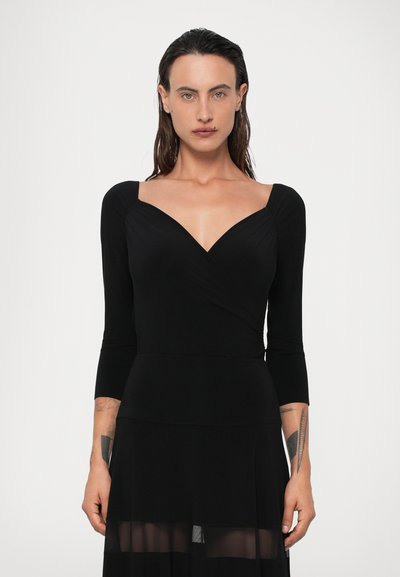 Schwarzes Kleid mit einem taillierten Oberteil, V-Ausschnitt und dreiviertel Ärmeln. Fließende, durchsichtige Skirt-Schicht sorgt für Textur und Bewegung.