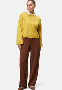 Pull en maille jaune avec col blanc, associé à un pantalon marron ample. Texture douce et coupe décontractée, adapté pour un style décontracté.