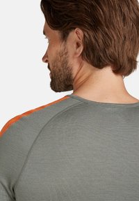 Grön träningsskjorta med orange axel detaljer, tillverkad av strukturerad tyg, med rundad halsringning och figurnära design.