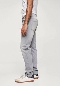 Jeans de mezclilla gris claro con un corte recto, que cuentan con cinco bolsillos y detalles de costura mínimos, combinados con zapatillas blancas y azul marino.