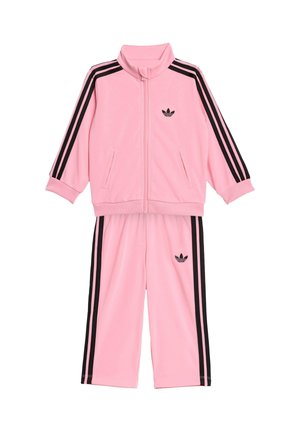 Różowy dres dziecięcy Adidas z czarnymi trzema paskami na rękawach i spodniach, kurtka na zamek oraz logo Adidas trefoil na piersi i nogawce.