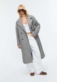 Grijze wolmix overjas met een dubbelzijdig ontwerp, grote revers en zwarte knopen, gecombineerd met een witte crop top en witte wijde broek.