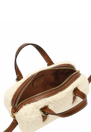Poignées et accents en cuir brun sur un sac en fausse fourrure de couleur crème. L'intérieur présente une doublure brune et une fermeture éclair dorée.
