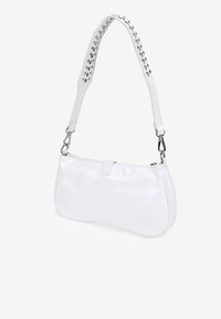 Bolso de mano de piel blanca con una textura suave, una forma estructurada y una correa ajustable con tachuelas. Cuenta con un cierre de cremallera y un mínimo de herrajes.