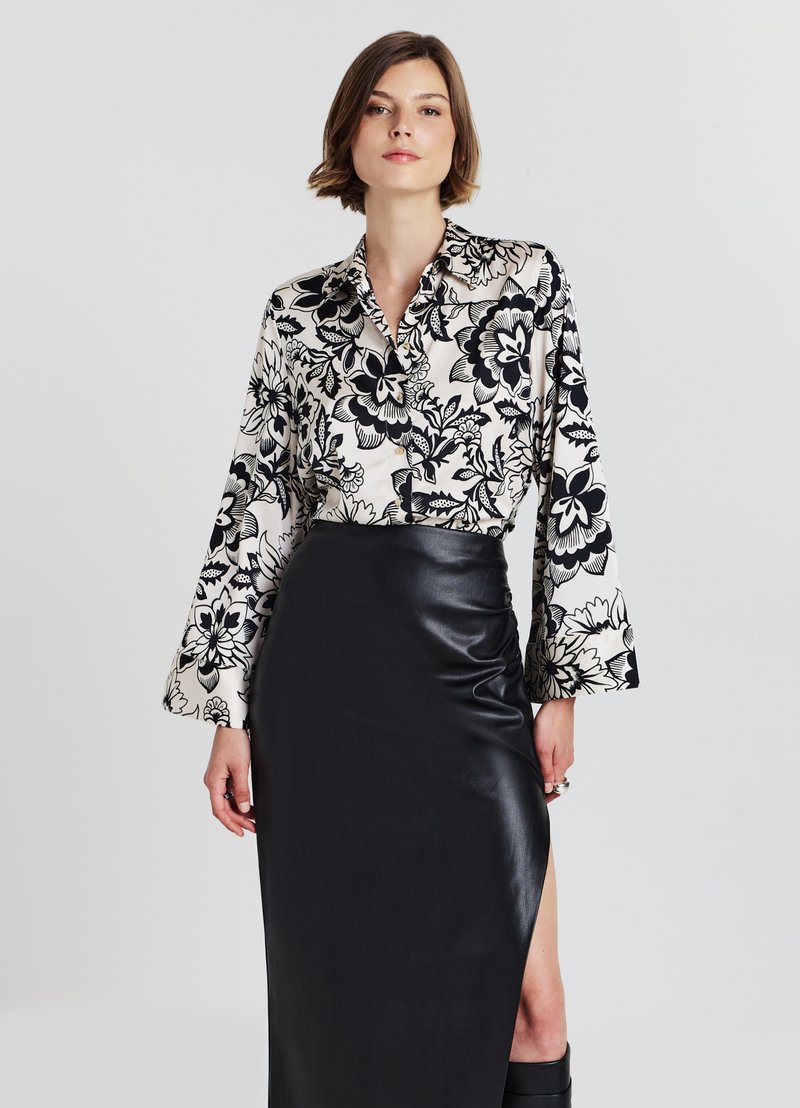 Black and white floral patterned blouse with long sleeves, paired with a sleek black leather skirt featuring a high slit. Smooth textures.