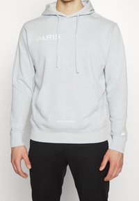 Sudadera gris claro con un bolsillo frontal. Presenta el texto blanco "PARÍS" en el pecho y "SAINT-GERMAIN" en el dobladillo. Tejido suave, diseño de tipo pullover.