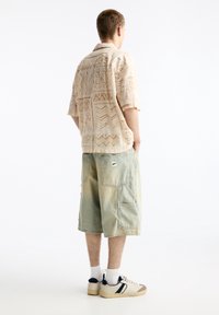 Korte mouw beige gekleedhemd met patroon, gecombineerd met lichtblauwe denim cargoshorts. Afgewerkt met witte en marineblauwe sneakers met een textuurdesign.