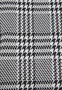 Svartvitt vävt tyg med ett hundtands- och zickzackmönster. Texturen är slät med en strukturerad design.