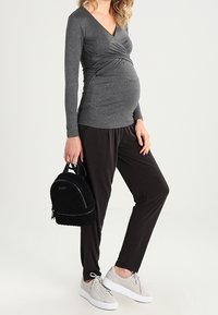 Graues langärmliges Oberteil mit V-Ausschnitt und gerafften Details, kombiniert mit schwarzen, lockeren Hosen und grauen Turnschuhen, dazu eine schwarze Mini-Rucksack.