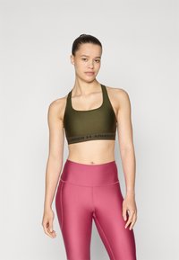 Grønn sports-bh med svart kant med "UNDER ARMOUR" tekst; parret med høyt liv, blanke rosa leggings. Glatt tekstur, tettsittende design.