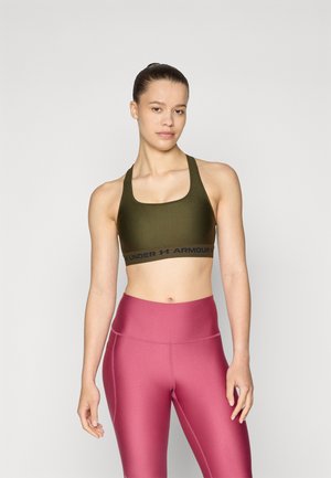 Zelena sportska grudnjak s crnim pojasom na kojem stoji natpis "UNDER ARMOUR"; uparen s visokim, sjajnim ružičastim tajicama. Glatka tekstura, uski kroj.