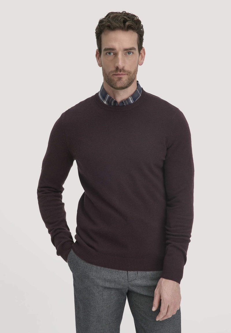 Bordeauxfarbenes Rundhals-Pullover aus weichem Strickmaterial, mit langen Ärmeln, gerippten Bündchen und Saum, getragen über einem blau-grauen Karierten Hemd.
