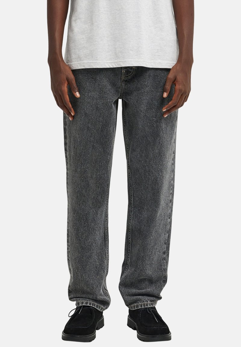 Musta farkut, joissa on haalistunut viimeistely, suora lahkeen malli ja viiden taskun tyyli. Yhdistetty harmaaseen t-paitaan ja mustiin kenkiin.