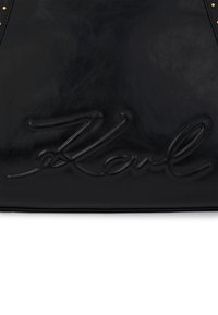 Czarna skórzana torba z wytłoczonym podpisem "Karl" i złotymi ćwiekami w górnych rogach.