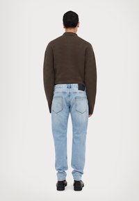Brown textured sweater with a high collar, paired with light blue denim jeans featuring a classic five-pocket design and black leather shoes.