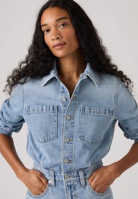 Ανοιχτό μπλε πουκάμισο από τζιν με κουμπιά μπροστά, δύο τσέπες στο στήθος και μανίκια που έχουν τυλιχτεί. Μαλακή υφή και άνετη εφαρμογή, με ορατή λεπτομερή ραφή.