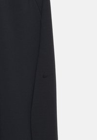 Μανίκι μαύρου αθλητικού φούτερ από ομαλό ύφασμα, με διακριτικό μαύρο λογότυπο της Nike στο πάνω μέρος του βραχίονα. Απλός, εφαρμοστός σχεδιασμός.