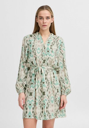 Robe à manches longues en tissu léger arborant un motif ikat vert et bleu, avec un décolleté en V et une ceinture en tissu à la taille.