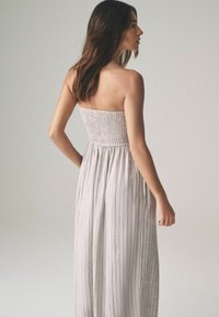 Strapless, wit gestreepte maxi-jurk met een smock-bodie en een vloeiende rok. Heeft verticale lijnen en een zachte, lichte stof.