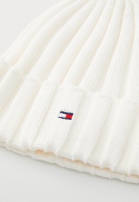 Biała dziana czapka beanie z żebrową fakturą. Posiada małe haftowane logo w kolorze granatowym, czerwonym i białym na mankiecie. Miękki, elastyczny materiał.