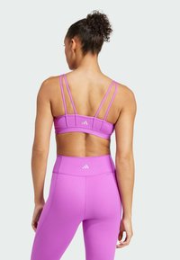 Sujetador deportivo morado con múltiples tirantes delgados, que presenta una textura suave y acentos de logotipo. Leggings morados de cintura alta completan el atuendo.
