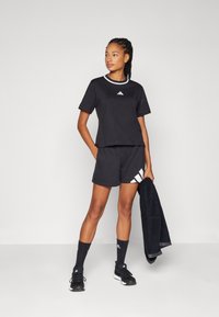 Μαύρη αθλητική ενδυμασία με κοντομάνικο τοπ με λευκό γιακά και λογότυπο, συνδυασμένη με σορτς και μαύρες κάλτσες. Απαλή υφή υφάσματος.