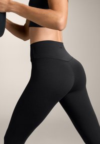 Czarne legginsy z wysokim stanem wykonane z elastycznego materiału, z gładką teksturą i dopasowanym krojem, podkreślające nogi i pośladki.