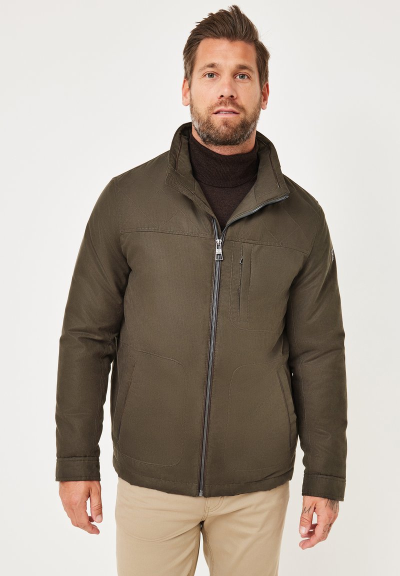 Olivgrüne Jacke mit durchgehendem Reißverschluss, hohem Kragen und zwei Seitentaschen. Strukturierter Stoff mit sichtbaren Nähten.