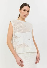 Vit stickad ärmlös topp med blommönster, med en lös passform och texturerad nät-design. Kombineras med en underdel i liknande textur.