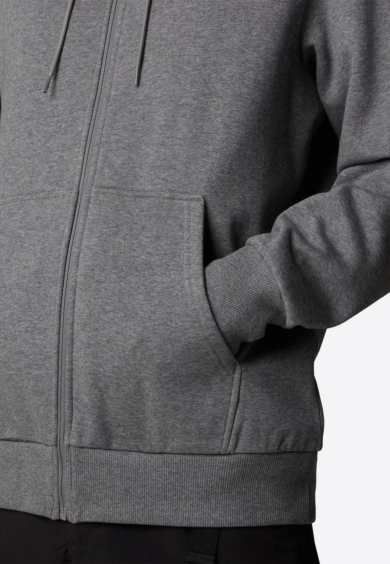 Sudadera gris con cremallera hecha de una tela suave, con puños y dobladillo acanalados, que incluye bolsillos tipo canguro y cordones para un ajuste personalizado.