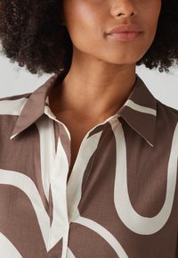 Brown and cream patterned shirt with a pointed collar, featuring a subtle sheen and smooth texture, showcasing flowing, organic shapes.