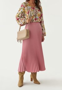 Falda plisada rosa combinada con una blusa floral con mangas abullonadas y un bolso cruzado beige. Botas de ante color topo hasta la rodilla.