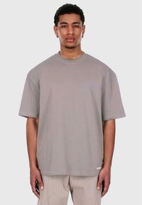 Grå oversized t-skjorte, kort erm, rund halslinje, laget av myk stoff. Har et lite merke ved kanten. Modellen står mot en enkel bakgrunn.