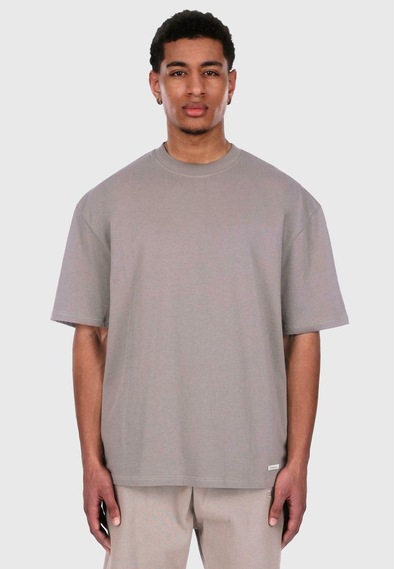 Grå oversized t-skjorte, kort erm, rund halslinje, laget av myk stoff. Har et lite merke ved kanten. Modellen står mot en enkel bakgrunn.