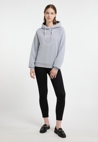 Szürke kapucnis felső, húzózsinórral, kör alakú grafikai designnal. Fekete skinny farmernadrággal és loaferekkel párosítva. Egyszerű és hétköznapi megjelenés.