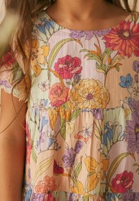 Abito floreale con uno sfondo pastello, realizzato in tessuto leggero e con un design a strati. I colori notevoli includono fiori rosa, gialli e viola.