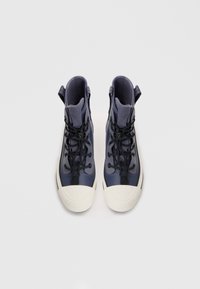Zapatillas altas en azul marino con un acabado texturizado, que cuentan con cordones negros, punteras de goma blanca y tiradores en el cuello.
